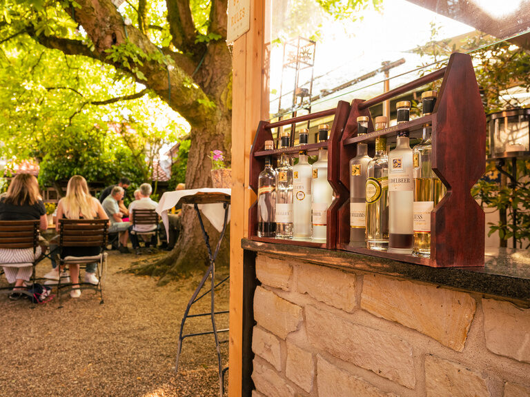 Personen genießen ihre Freizeit unter einem Baum im Biergarten, umgeben von Tischen und Stühlen.